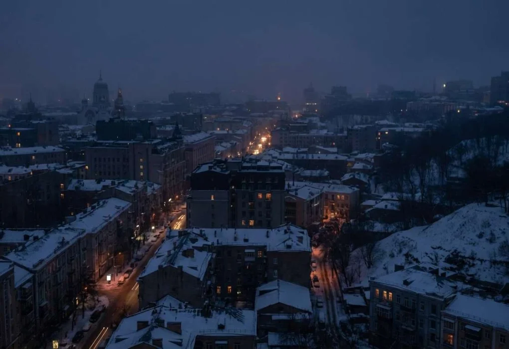 A night view of Kyiv during a winter power outage, showing darkened buildings with a few visible lights, created as an AI-generated illustration representing recent electricity losses after strikes.