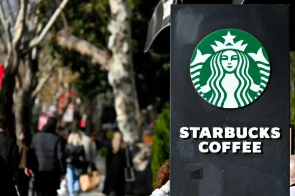 Starbucks outdoor sign with pedestrians walking past on a busy street.
