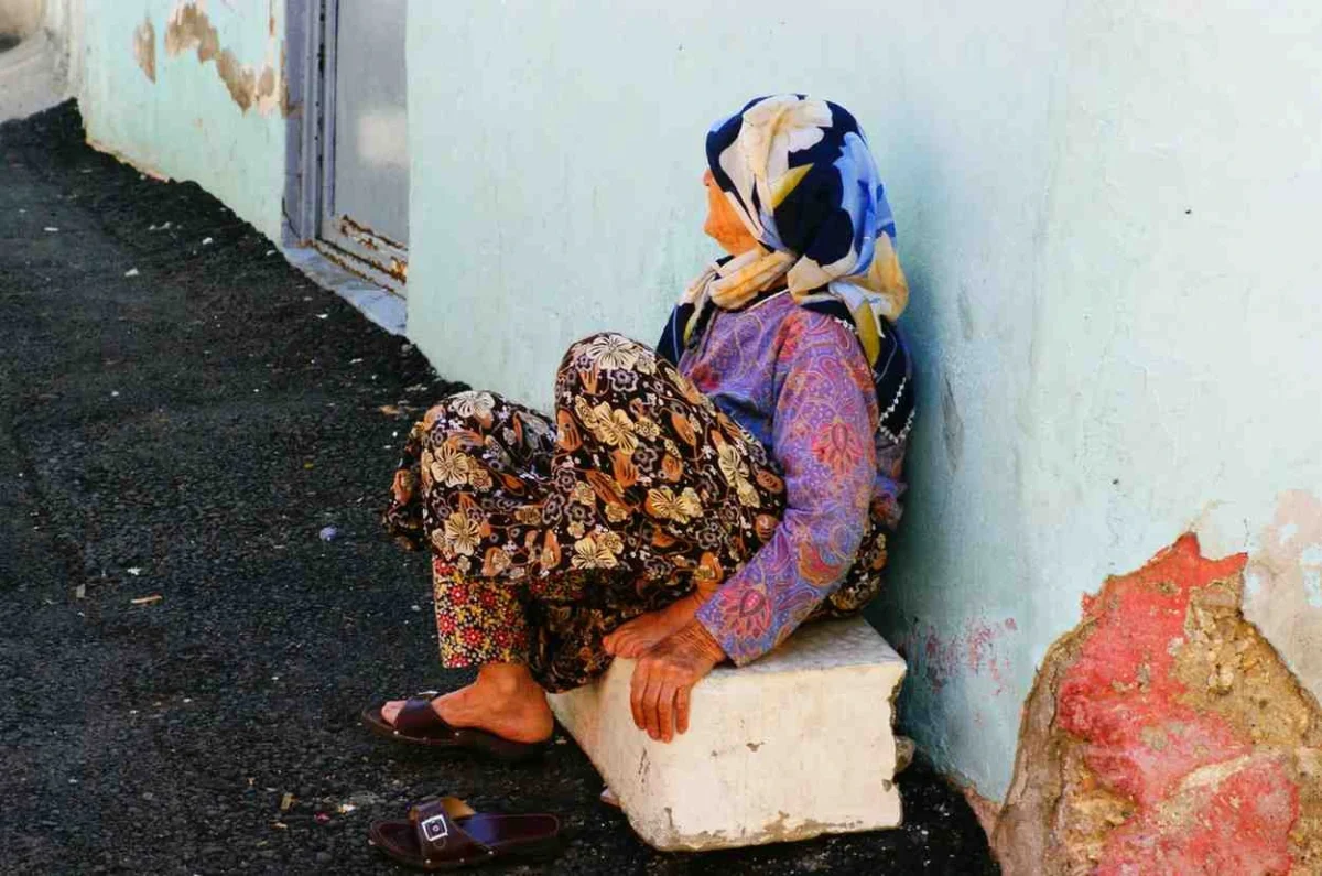 Illustrative image of an elderly woman sitting outside a building, reflecting the uncertainty faced by Syrians displaced by years of conflict.