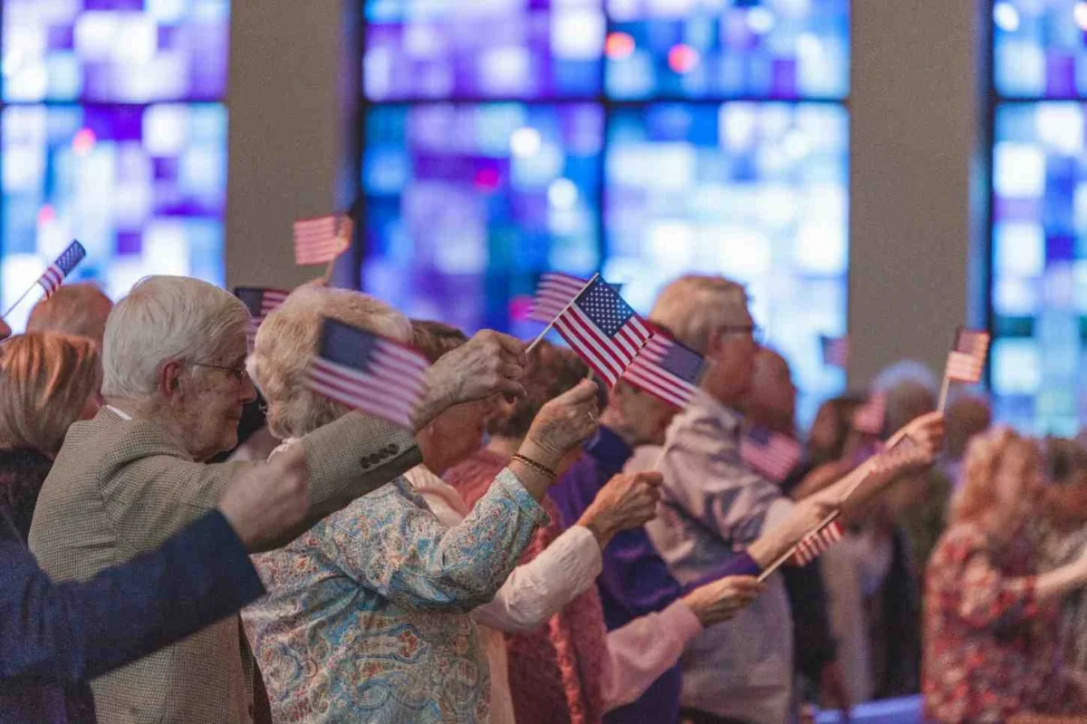 People waving small American flags during a U.S. naturalization ceremony, reflecting halted citizenship processes.
