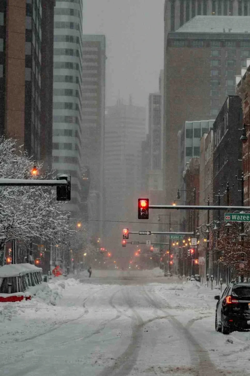 Snow-covered city street during an extreme winter storm in the United States, with heavy snowfall, low visibility, and icy road conditions