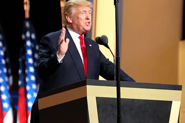 Donald Trump speaking at a podium with American flags in the background