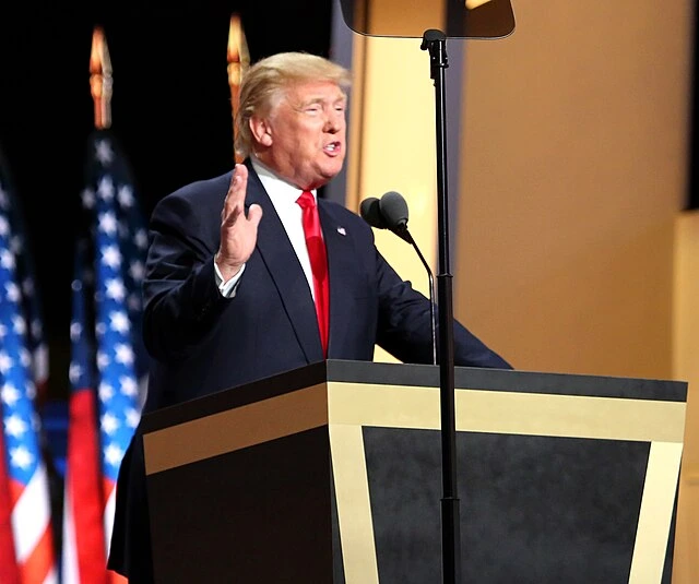 Donald Trump speaking at a podium with American flags in the background