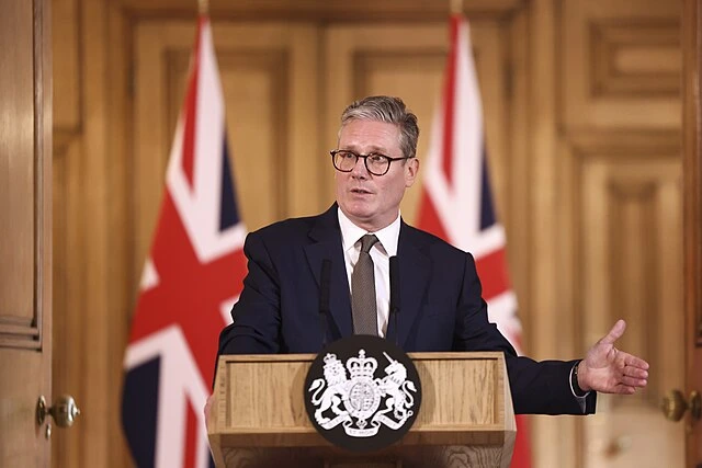 UK prime minister speaking at an official podium with Union Jack flags during a government address